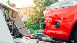 Nahaufnahme eines roten Autos im Profil, das gerade auf einen weissen Abschleppwagen gezogen wird