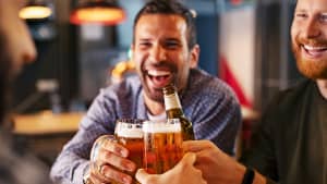 Drei Männer, mittleren Alters, stoßen in einer Kneipe mit Bier an