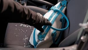 Ein Einbrecher greift durch eine zerbrochene Scheibe in ein Auto und klaut eine Handtasche