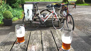 Zwei Biergläser stehen auf einem Tisch, im Hintergrund sind zwei Fahrräder zu sehen