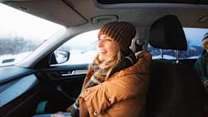 Eine junge Frau die mit einem Wintermantel auf dem Beifahrersitz im Auto sitzt