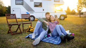 Pärchen sitzt vor einem Wohnmobil und macht ein Selfie