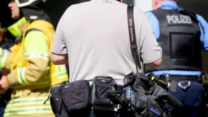 Ein sogenannter Blaulichtreporter steht während eines Feuerwehreinsatzes hinter einem Feierwehrmann und einem Polizisten.