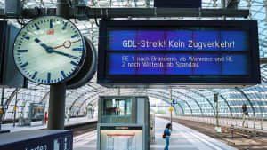 Auf einem Display steht „GDL-Streik – kein Zugbetrieb“, während ein Fahrgast während eines Warnstreiks im Bahnbetrieb in Deutschland am Berliner Hauptbahnhof auf einem fast menschenleeren Bahnsteig wartet