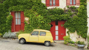 Gelber Renault R4 parkt vor einem weinbehangenen Haus in Frankreich