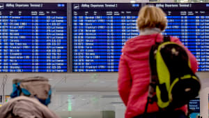 Eine Frau schaut auf eine Anzeigetafel für die Abflüge am Flughafen München.