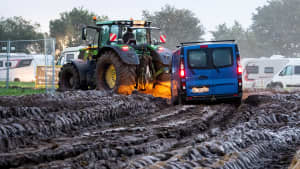 Ein Auto wird von einem Traktor abgeschleppt auf dem Wacken Open Air Festival 2023 bei Matsch und Regen