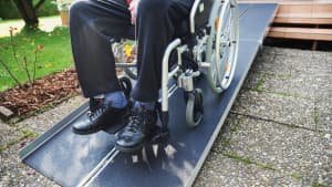 Ein Rollstuhlfahrer der mit Hilfe einer Rampe eine erhöhte Eingangstüre runter fahren kann