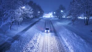 ein Auto fährt Nachts auf verschneiter Strasse