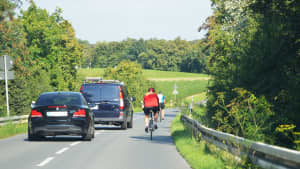 Zwei Autofahrer überholen zwei Radfahrer auf einer Landstraße