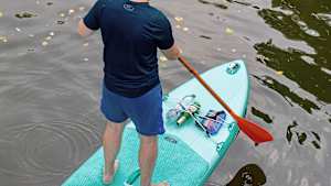 Ein Mann steht auf einem SUP, in der Halterung sind eine Wasserflasche und eine Bierflasche eingeklemmt