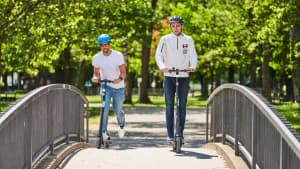 Zwei Männer fahren auf zwei E-Scooter über eine Brücke