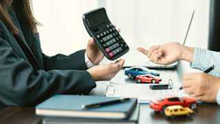 Eine Person präsentiert einen Taschenrechner, eine andere Person füllt ein Formular aus zum Auto finanzieren