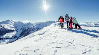 Eine Familie mit Skiern im Schnee im Hintergrund sieht man die Kitzbühler Alpen