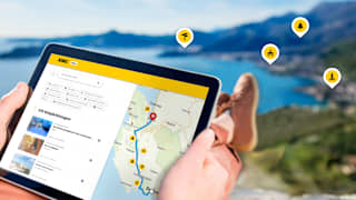 Ein Mann sitzt mit seinem tablet im Urlaub auf einem Berg