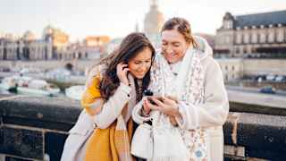 Zwei frauen schauen auf ein Mobiltelefon und lachen gemeinsam