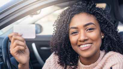 Junge lächelnde Frau sitzt im Auto und hält ihren Führerschein hoch