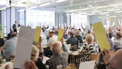 Mitglieder des ADAC Nordbaden sitzen im Saal und heben Wahlzettel für eine Abstimmung nach oben