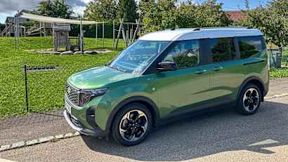 Ford Tourneo E-Courier stehend neben einer Wiese, Seitenansicht.