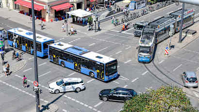 Verschiedene Verkehrsteilnehmer wie Autofahrer, Straßenbahn, Bus, Fußgänger und Radfahrer fahren über eine Kreuzung