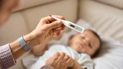 Ein kleines Kind liegt & die Mutter hält gerade ein Fieberthermometer in der Hand