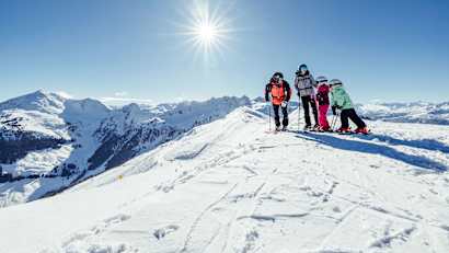 Eine Familie mit Skiern im Schnee im Hintergrund sieht man die Kitzbühler Alpen