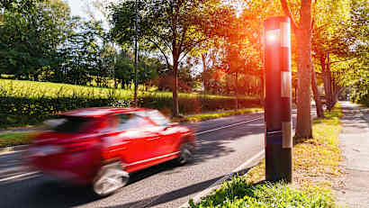 Rotes Auto an einer sommerlichen Landstrasse, das gerade geblitzt wird