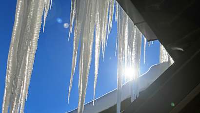 Lange Eiszapfen an einem Häuserdach glänzen im Sonnenlicht