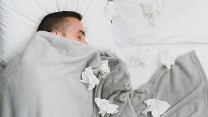 Ein Mann liegt mit vielen benutzen Taschentüchern krank im Bett