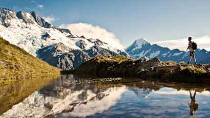 Ein Wanderer läuft an einem See vorbei, im Hintergrund sieht man schneebedeckte Berge.