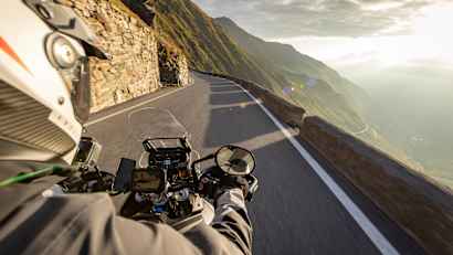 Motorradfahren in den italienischen Alpen bei Sonnenaufgang, Blick vom Lenker, dramatischer Himmel. Reisen und Freiheit, Aktivitäten im Freien