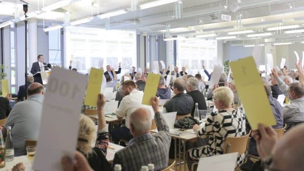 Mitglieder des ADAC Nordbaden sitzen im Saal und heben Wahlzettel für eine Abstimmung nach oben
