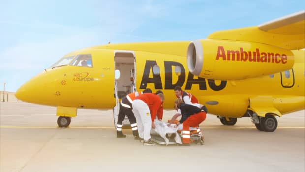 Ein ADAC-Ambulance-Flugzeug steht auf einem Rollfeld. Die Kabinentür steht offen, da ein Patient durch das Rettungspersonal ins Flugzeug gebracht werden soll für einen Krankenrücktransport.