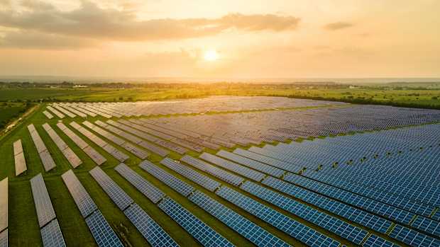 Ein Solarkraftwerk auf einem grünen Feld bei Sonnenuntergang, mit Reihen von Solarpaneelen, die die Sonnenenergie nutzen zu dem aktuellen Stromtarif.
