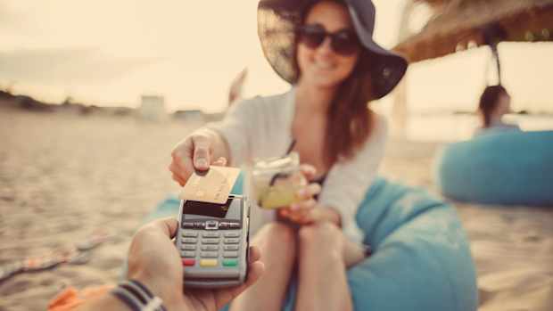 Eine Frau sitzt am Strand und bezahlt ihren Cocktail mit einer debitkarte oder kreditkarte