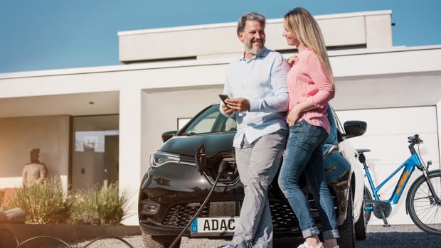 Paar steht vor ladendem E-Auto und E-Bike