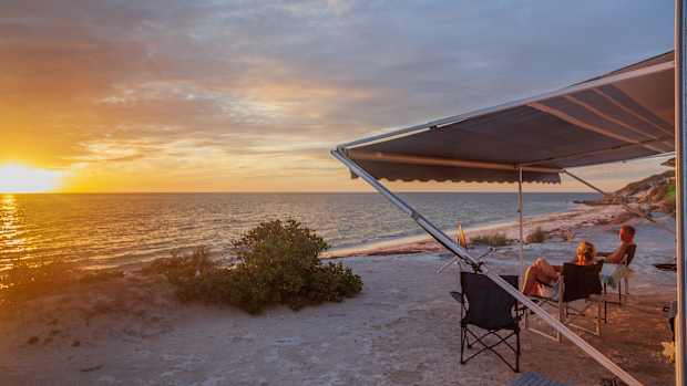 Ein Mann und eine Frau genießen an einem Strand den Sonnenuntergang, denn in man kann jetzt in Australien Camper mieten