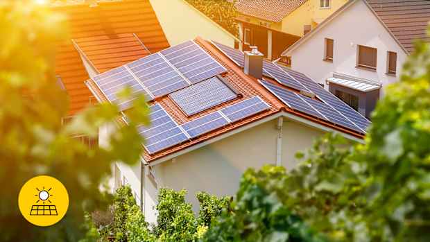 Ein Einfamilienhaus mit Solarpaneelen auf dem Dach, umgeben von grüner Vegetation, in einer sonnigen Wohngegend wurde durch eine energetische Sanierung verbessert.