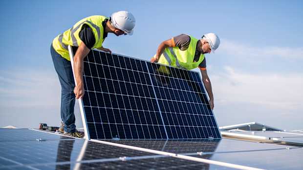 Zwei Handwerker installieren eine PV-Anlage auf einem Dach