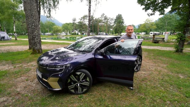 Mr. Ride steigt aus einem schwarzen E-Auto aus auf einem Campinggelände und zeigt auch mit einem E-Auto Camping funktioniert einwandfrei.