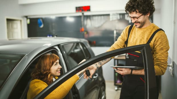 Frau sitzt in grauem Auto und übergibt Schlüssel an Mann bei einer Wartung Leasing-Auto