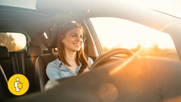 Frau sitzt hinter dem Steuer eines Autos bei Sonnenuntergang und lächelt, weil sie durch die GAP-Versicherung beim Leasing total abgesichert ist.