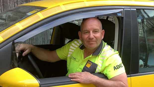 Ein ADAC-Mitarbeiter sitzt in einem gelben Auto und ist bereit, Autofahrern bei einer Panne im Ausland zu helfen.