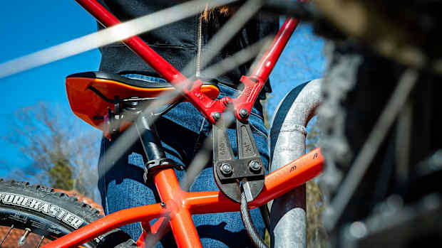 Eine Person schneidet mit einem Bolzenschneider ein Fahradschloss von einem orangem Fahrrad auf, ein weiterer Grund für eine Fahrradversicherung