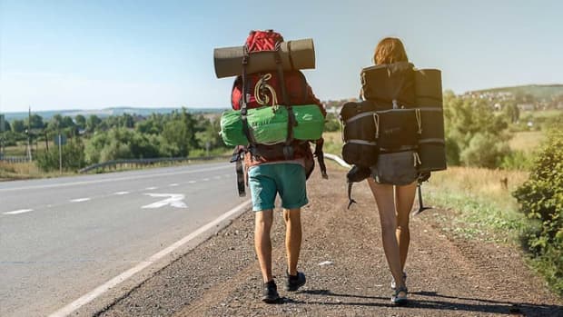 Zwei Rucksacktouristen gehen am Rande einer Straße entlang und sind unbeschwert, weil sie einen ADAC Auslandskrankenschutz Langzeit haben