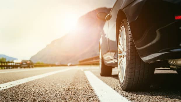 Ein schwarzes Auto steht im Sonnenschein auf dem Pannenstreifen, deshalb ist eine gute Autoversicherung ein Muss.