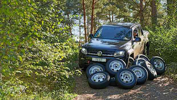 ADAC Ingenieur Christoph Pauly sitzt in einem Auto, vor dem Auto sind verschiedene All Terrain Reifen abgelegt