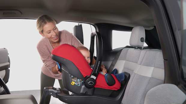 Eine Frau befestigt ihr Kind mit einer Babyschale auf der Rückbank eines Autos