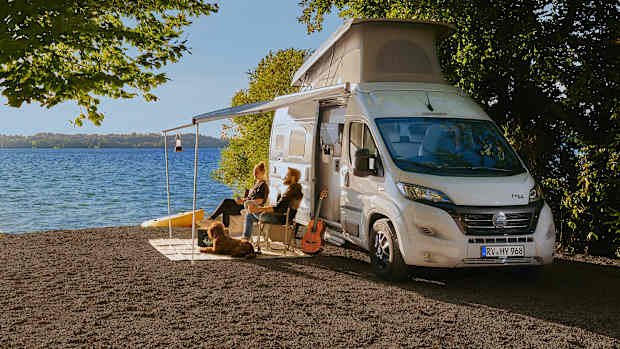 Menschen sitzen vor ihrem Wohnmobil an einem See