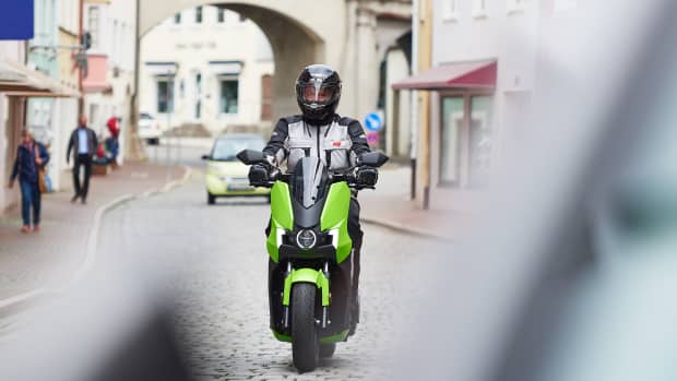 Ein E-Vespa Fahrer fährt mit Schutzkleidung auf einer Straße